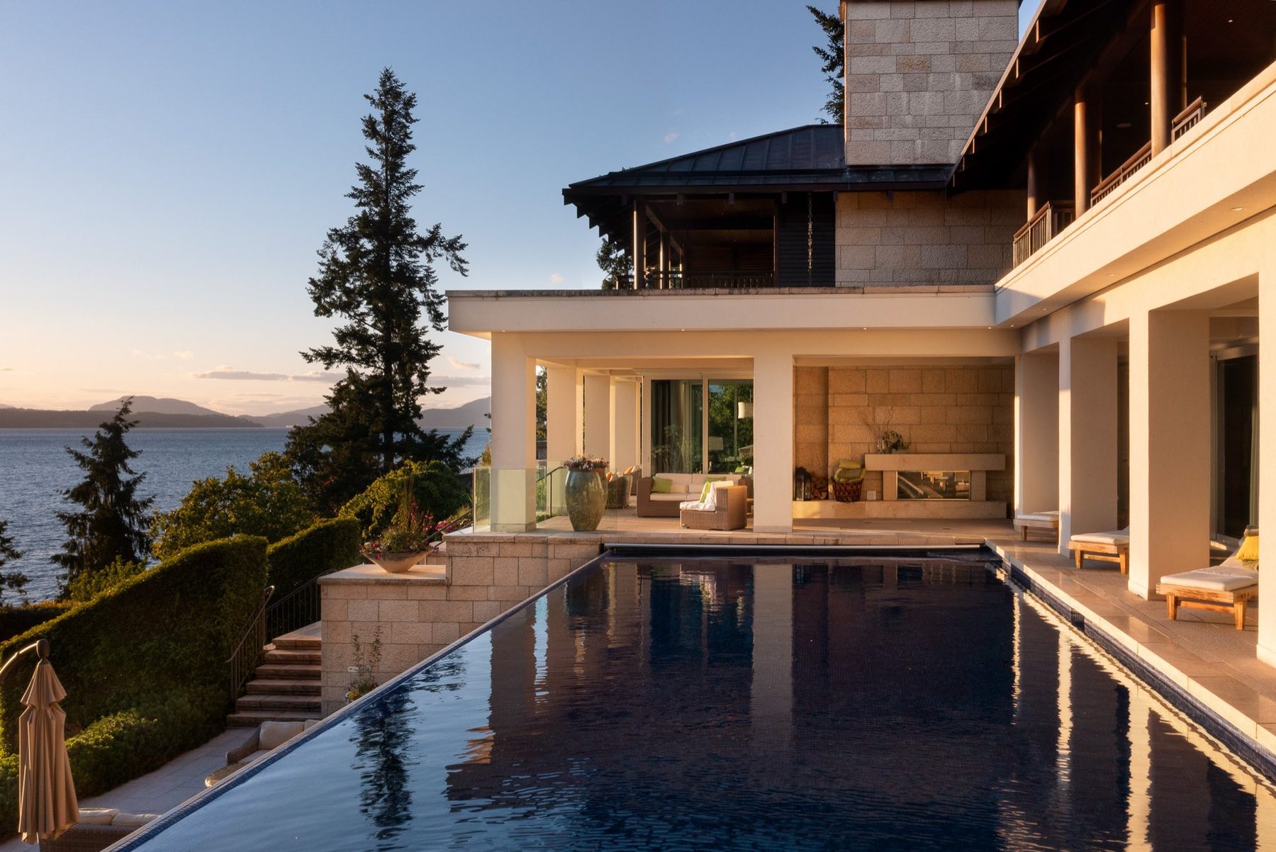 Infinity pool at golden hour beside a stone and timber home overlooking the ocean