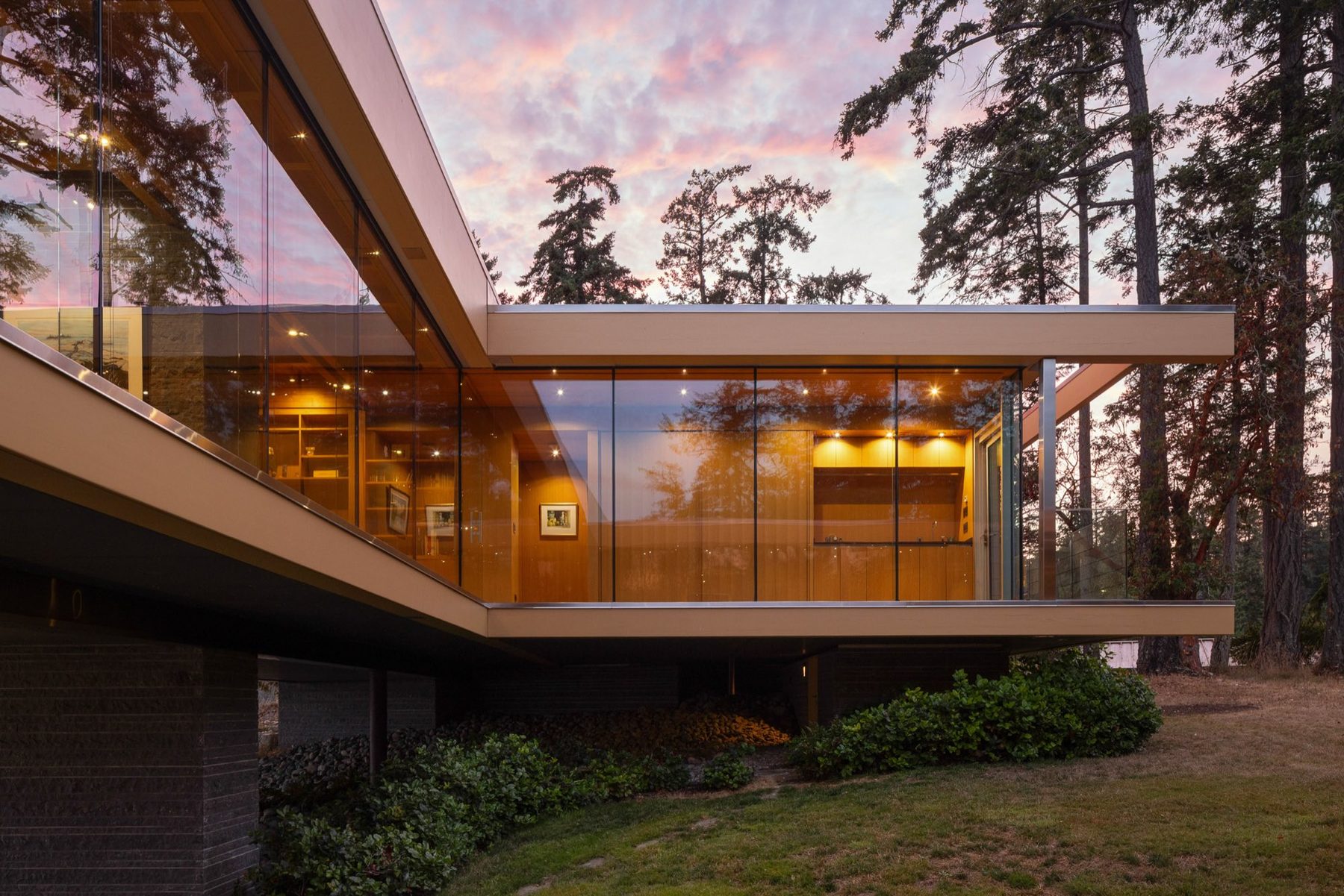 Glass pavilion glowing at dusk under a pink and violet sky